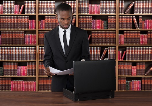man standing in front of his desk in a library with an open suitcase holding documents