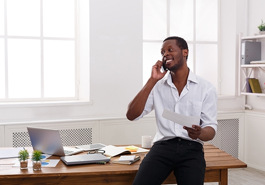 man leaning on his desk talking on his cell phone