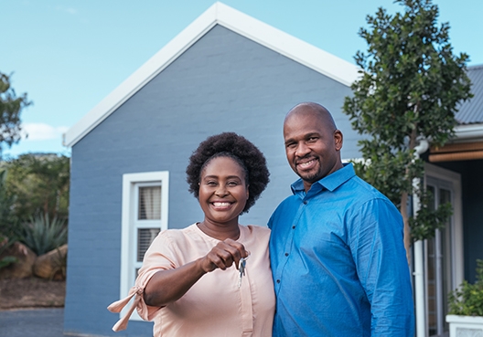 couple holding house keys standing in from of a house